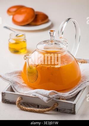 Thé vitaminé chaud d'argousier dans une petite théière en verre avec des baies d'argousier fraîches crues et du miel. Boisson saine de saison. Mise au point sélective Banque D'Images