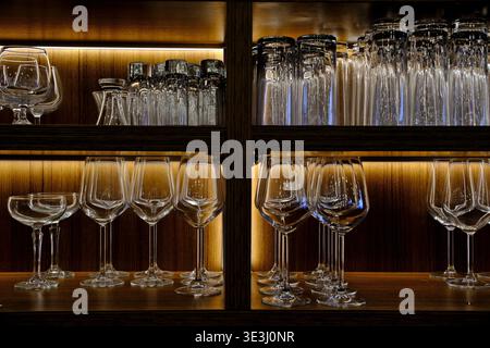 Grossissement de divers verres à vin sur une étagère en bois dans un bar, éclairés d'une lueur chaude, intérieur de restaurant Banque D'Images