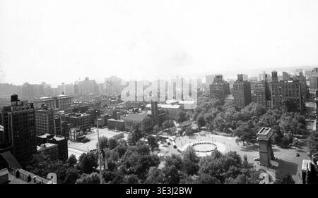 Cette photographie vintage en noir et blanc réalisée par Angelo Rizzuto dans les années 1950 capture une vue panoramique du Washington Square Park à New York. L'emblématique Washington Square Arch est visible au premier plan, entourée d'arbres luxuriants et du paysage urbain dense de Greenwich Village. Banque D'Images