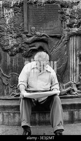 Un homme âgé, capturé par le photographe Angelo Rizzuto probablement dans les années 1950 ou 1960, est plongé dans la lecture alors qu'il est assis à la base de l'Independence Flagstaff dans Union Square Park. Le monument, inscrit avec un texte commémorant le 150e anniversaire de la Déclaration d'indépendance en 1926, fournit une toile de fond historique à cette scène de photographie de rue représentant un moment de la vie quotidienne dans la ville vintage de New York. Banque D'Images