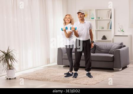 Homme mûr et femme tenant des haltères et posant dans un salon Banque D'Images