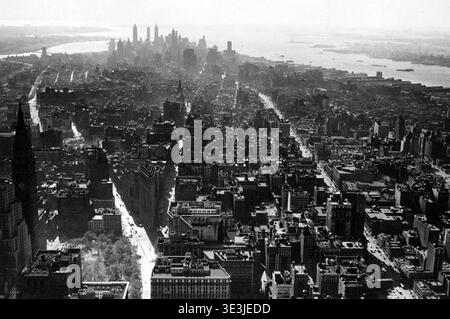 Cette superbe photographie aérienne en noir et blanc capture une vue panoramique du paysage urbain de Manhattan vers le sud, probablement des années 1930 ou 1940 Angelo Rizzuto, le photographe, présente habilement le paysage urbain dense avec les gratte-ciel du quartier financier et la lointaine Statue de la liberté. Cette image offre un aperçu de la grandeur architecturale vintage de New York et de ses rues animées avant les explosions ultérieures de la construction. Banque D'Images