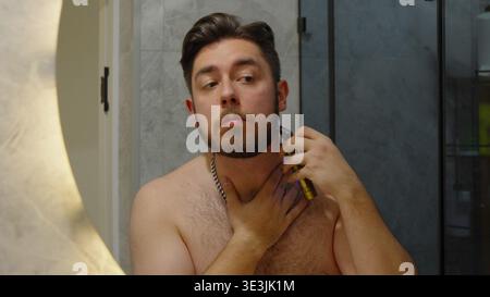 Homme regardant son reflet en se rasant le visage dans la salle de bain Banque D'Images