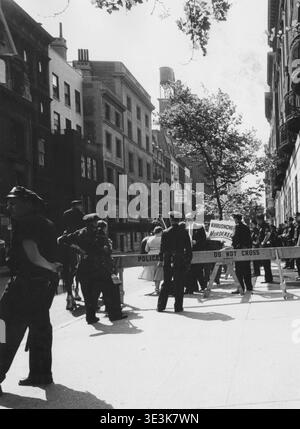Cette photographie de rue vintage, probablement capturée par Angelo Rizzuto dans les années 1960, représente une barrière de police gérant une manifestation ou un rassemblement public à New York. De nombreux policiers se tiennent à côté de barricades en bois marquées « POLICE DEPT ». Et "NE PAS TRAVERSER", tandis qu'un panneau disant "MEURTRIER DE KHROUCHTCHEV" est visible en arrière-plan, offrant un aperçu du climat politique de l'époque. Banque D'Images