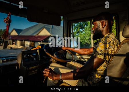 PAJE, ZANZIBAR - 18 OCTOBRE 2025 : un Africain local conduisant un bus à travers un village de Zanzibar, capturé à la lumière chaude de l'heure d'or à travers le camion Banque D'Images