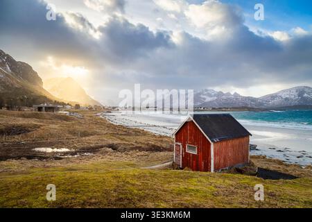 Cabane rouge typique sur la plage de Rambergstranda au coucher du soleil en hiver. Flakstadoya, Nordland, Lofoten, Norvège, Europe du Nord. Banque D'Images