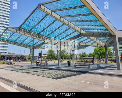 Une structure d'auvent architecturale moderne dans une place urbaine avec un cadre géométrique en métal avec des panneaux de verre translucides teintés en bleu disposés dedans Banque D'Images