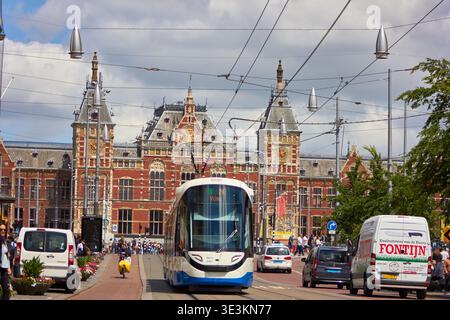Un tramway moderne blanc et bleu GVB parcourt les voies ferrées devant la gare centrale d'Amsterdam aux pays-Bas. Le chemin de fer historique en briques rouges Banque D'Images