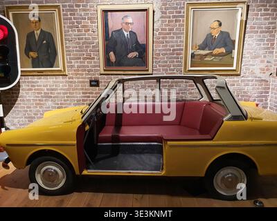 Une voiture cabriolet vintage jaune modifiée en un présentoir de canapé positionné à l'intérieur contre un mur de briques apparentes avec trois formels encadrés Banque D'Images
