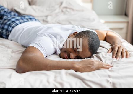 Jeune homme noir dormant paisiblement sur le lit dans la lumière du matin, se reposant confortablement Banque D'Images