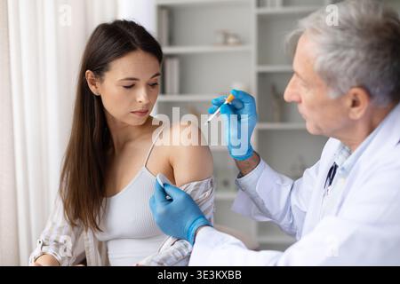 Médecin administrant l'injection de vaccin à la patiente en clinique Banque D'Images