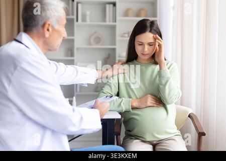 Femme enceinte souffrant de maux de tête pendant la consultation médicale pendant que le médecin fournit un soutien Banque D'Images