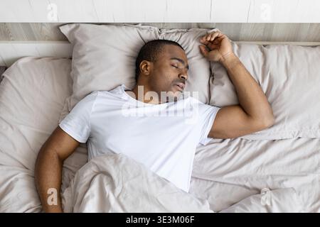 Jeune homme noir dormant paisiblement dans son lit pendant la journée, posture détendue Banque D'Images