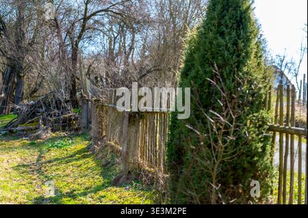 Ancienne clôture en bois menant à travers le jardin rural avec la lumière du soleil et des arbres, scène de campagne paisible, concept de direction, limite, voyage et traditi Banque D'Images