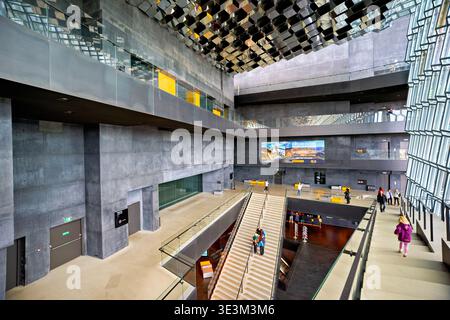 Les visiteurs se promènent dans l'opéra Harpa. L'architecture moderne montre de grands panneaux de verre et des espaces ouverts. Les gens sont vus apprécier le lieu. Banque D'Images
