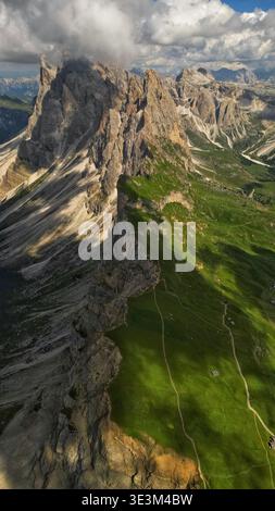 Vue aérienne des pics rocheux accidentés contrastent fortement avec les prairies verdoyantes sous un ciel nuageux, Seceda, Italie. Banque D'Images