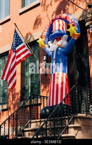 Grande figure gonflable de l'oncle Sam sur un porche devant un bâtiment en brique avec un drapeau américain montrant l'esprit de célébration du quatrième juillet Banque D'Images