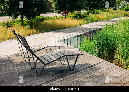 Deux chaises en bois vides placées sur une promenade par un petit plan d'eau entouré de verdure dans un cadre de parc Banque D'Images