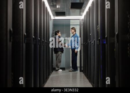 Jeune homme asiatique et homme caucasien d'âge moyen serrant la main dans la salle de serveur Banque D'Images