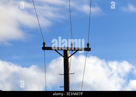 Poteau utilitaire en bois avec lignes électriques contre le ciel bleu et les nuages Banque D'Images