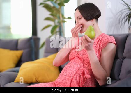 Moments joyeux d'une femme enceinte dégustant des fruits frais tout en se relaxant à la maison dans un cadre cosy Banque D'Images