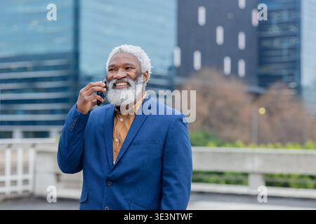 Homme afro-américain portant blazer parlant sur smartphone debout sur la terrasse du bureau Banque D'Images