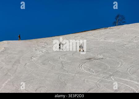 Les gens skient sur une pente de montagne avec des pistes courbes dans la neige par une journée ensoleillée Banque D'Images