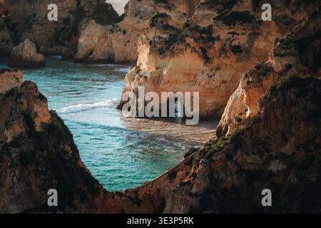 Vue sur les falaises escarpées embrassent la mer turquoise, sculptée avec des grottes cachées, tandis que la lumière du soleil danse sur la surface de l'eau, Alvor, Faro, Portugal. Banque D'Images