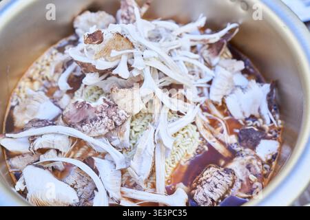Quatre photos montrent le processus de cuisson étape par étape du ramyeon de champignon de pin coréen dans un pot doré traditionnel, mettant en valeur un délice d'automne aromatique Banque D'Images