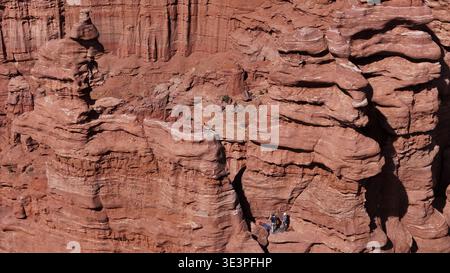 Vue aérienne de grimpeurs perchés sur une formation de grès, le rocher rouge contrastant avec le vaste ciel bleu, Moab, Utah, États-Unis. Banque D'Images