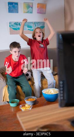 Les garçons encouragent leur équipe, réagissent émotionnellement à un match de football à la télévision avec des collations Banque D'Images