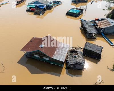 Vue aérienne des maisons sur pilotis s'élèvent des eaux boueuses, reflétant le ciel couvert, un témoignage de la vie adaptée au reflux et au débit du grand lac Banque D'Images