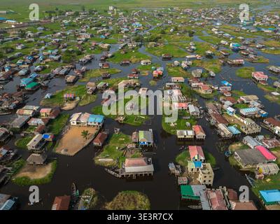 Vue aérienne de maisons sur pilotis s'élevant de l'eau, reflétant le ciel dans l'étreinte de la lagune, une tapisserie de vie tissée sur l'eau, Ganvié, Bénin. Banque D'Images