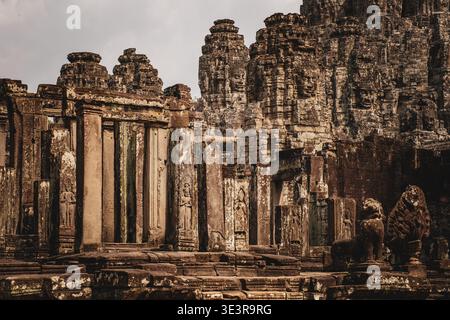 Tours de visage, colonnes de galerie sculptées et lion de pierre gardien du temple de Bayon, le temple d'État d'Angkor Thom, Siem Reap, Cambodge. Banque D'Images