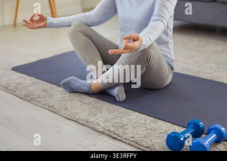 Femme senior méditant sur tapis de sport, pratiquant le yoga et faisant des exercices de respiration à la maison. Banque D'Images