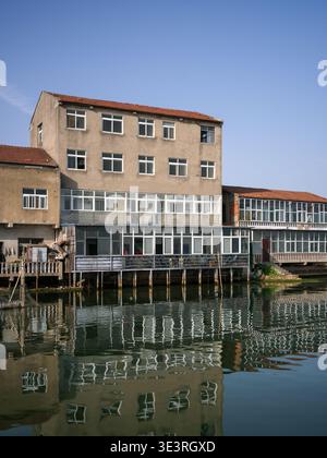 Ancien bâtiment de plusieurs étages avec une façade altérée et de nombreuses fenêtres construites directement sur l'eau, reflétant parfaitement la surface calme du lac sous-jacent Banque D'Images