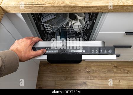 Porte de lave-vaisselle ouverte montée dans un meuble de cuisine blanc moderne intégré, comptoir en bois, meubles brillants, allumer le lave-vaisselle, pressin Banque D'Images