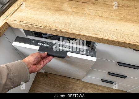 Porte de lave-vaisselle ouverte montée dans un meuble de cuisine blanc moderne intégré, comptoir en bois, meubles brillants, allumer le lave-vaisselle, pressin Banque D'Images