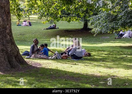 Les gens se détendent sur l'herbe dans un parc ensoleillé sous de grands arbres. Londres, Royaume-Uni, 23 juillet 2023 Banque D'Images