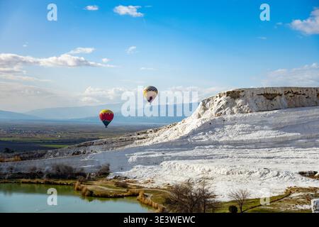 Les montgolfières dérivent au-dessus des terrasses en travertin uniques de Pamukkale, en Turquie. La journée lumineuse accentue les couleurs vibrantes des ballons agains Banque D'Images