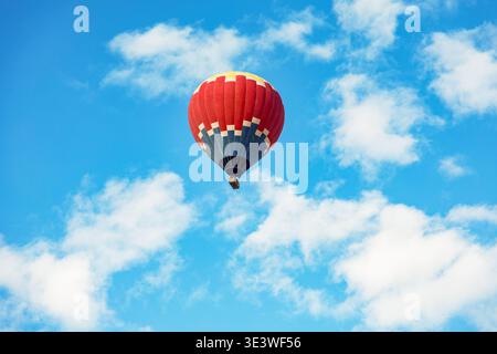 Une montgolfière rouge vif flotte gracieusement contre un ciel bleu vif parsemé de nuages blancs moelleux, symbolisant l'aventure, la liberté et explora Banque D'Images