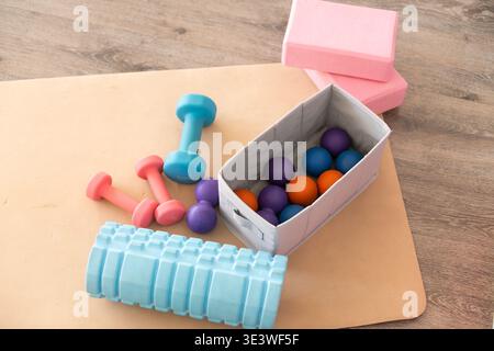 Une collection d'appareils de fitness à domicile sur un plancher en bois, avec des haltères colorés, des blocs de yoga, des balles de massothérapie, et un rouleau en mousse, parfait Banque D'Images