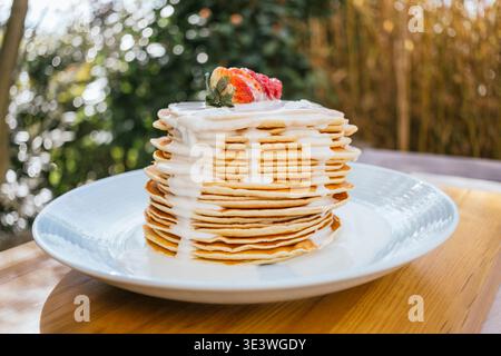 Une délicieuse pile de crêpes moelleuses garnies d'un délicieux filet de chocolat blanc et de fraises fraîches, parfaites pour un délicieux petit déjeuner ou un brunch Banque D'Images