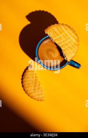 Une scène vibrante d'une tasse de café avec un expresso riche, partiellement recouverte d'un biscuit fendu sur un fond jaune vif, offrant un co chaleureux et accueillant Banque D'Images