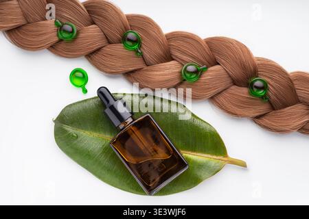 L'invention concerne un agencement présentant un sérum de soin capillaire dans des capsules vert vif placées sur une section de cheveux tressée avec un flacon compte-gouttes en verre sur une feuille verte, illu Banque D'Images
