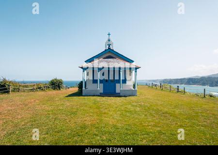 Ermitage pittoresque à Cadavedo, dans les Asturies, situé sur une herbe verte luxuriante avec une toile de fond magnifique de la mer et des collines ondulantes, mettant en valeur un cadre serein et image Banque D'Images