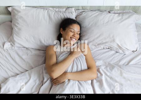 Femme noire couchée paisiblement dans son lit, les yeux fermés, souriants et détendus Banque D'Images