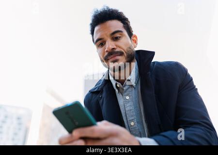 Jeune homme adulte latino-américain regardant un smartphone à l'extérieur Banque D'Images