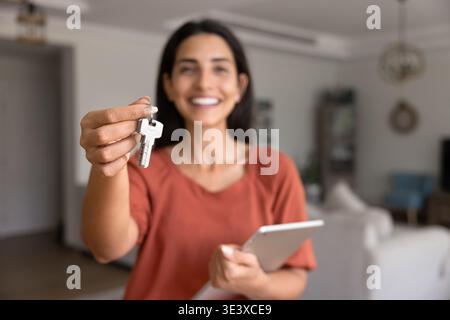 Femme souriante tenant les clés de la maison debout à l'intérieur Banque D'Images