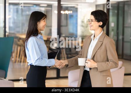 Deux collègues féminines multiethniques souriantes se serrant la main au bureau Banque D'Images